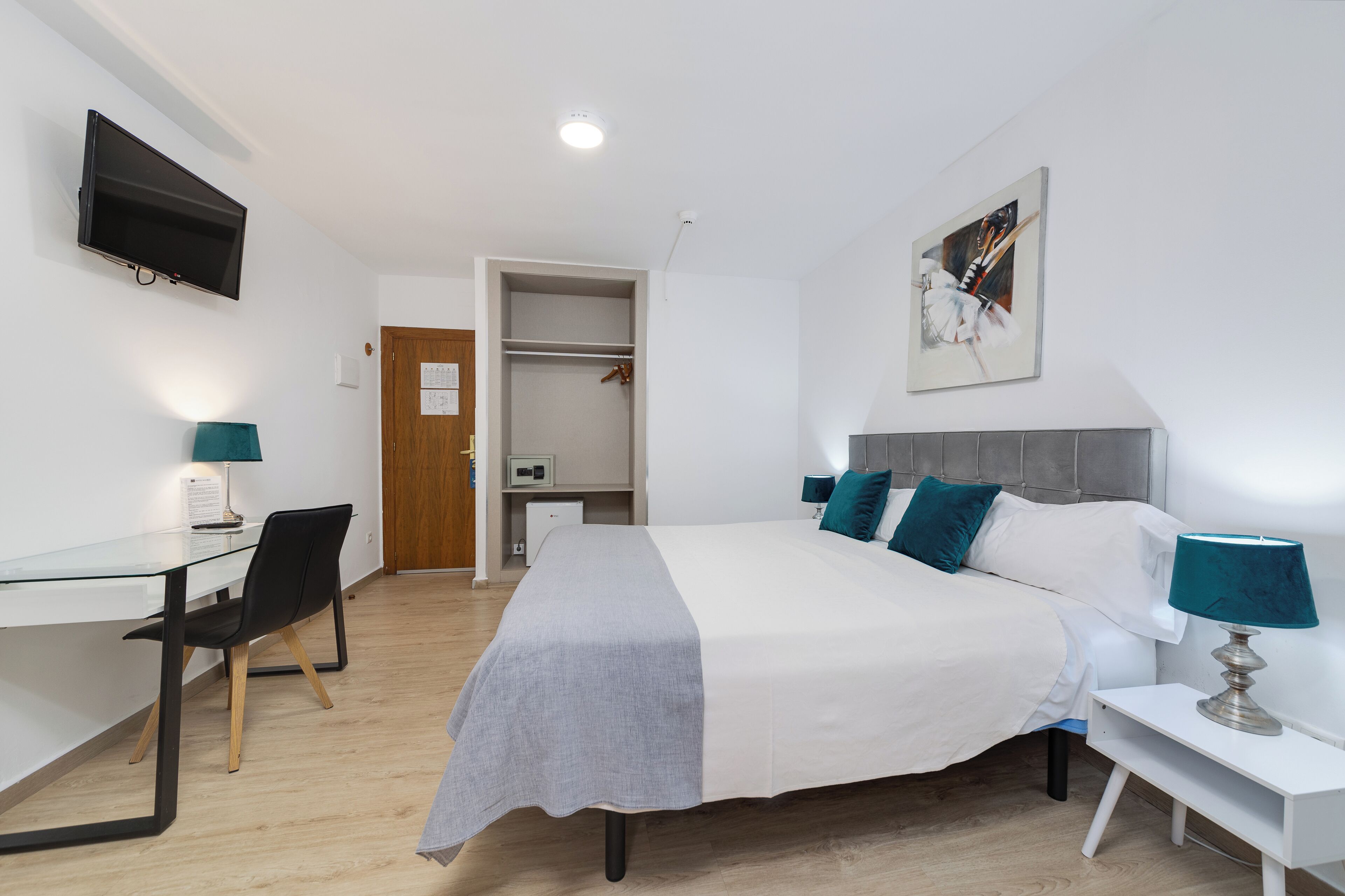 Una habitación de hotel moderna con cama, mesita de noche, escritorio, silla y televisión montada en la pared.