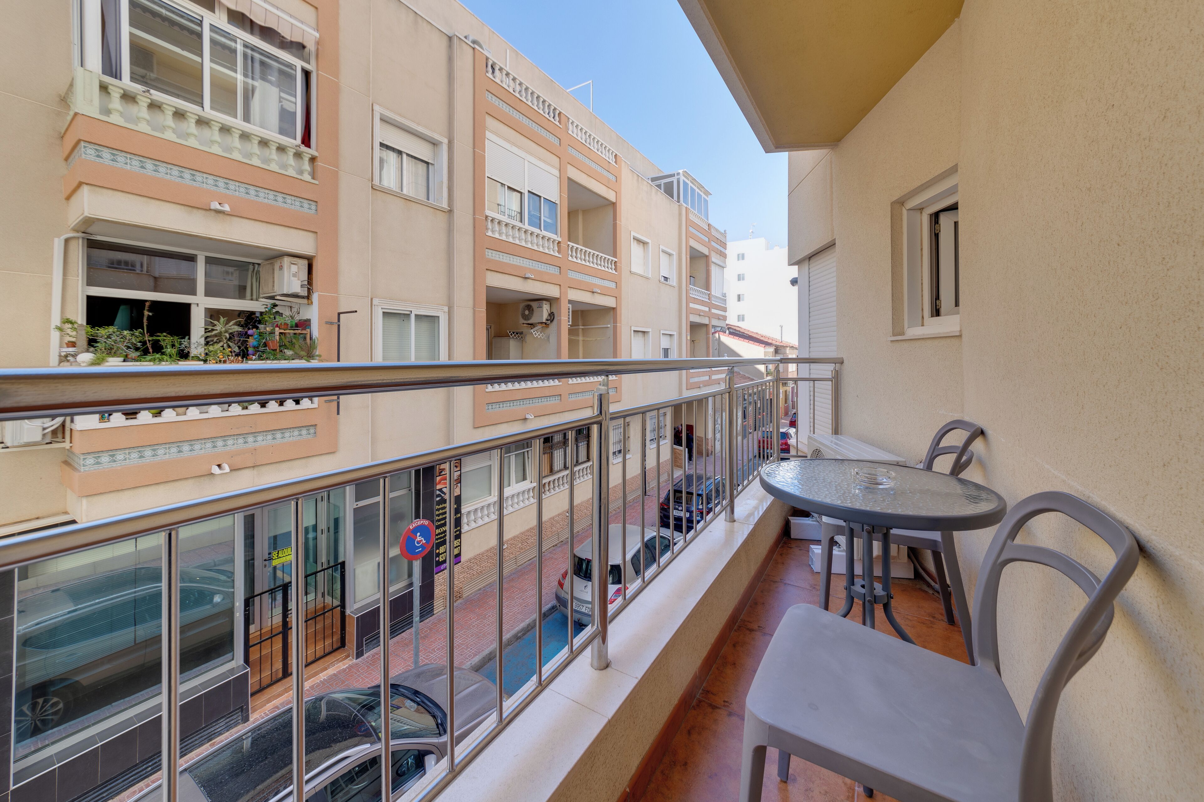 A balcony with a table and chairs, overlooking a street with cars and buildings.