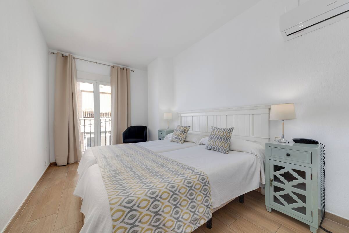 A hotel room with a large bed, a bedside table with a lamp, and a view of the outside balcony.