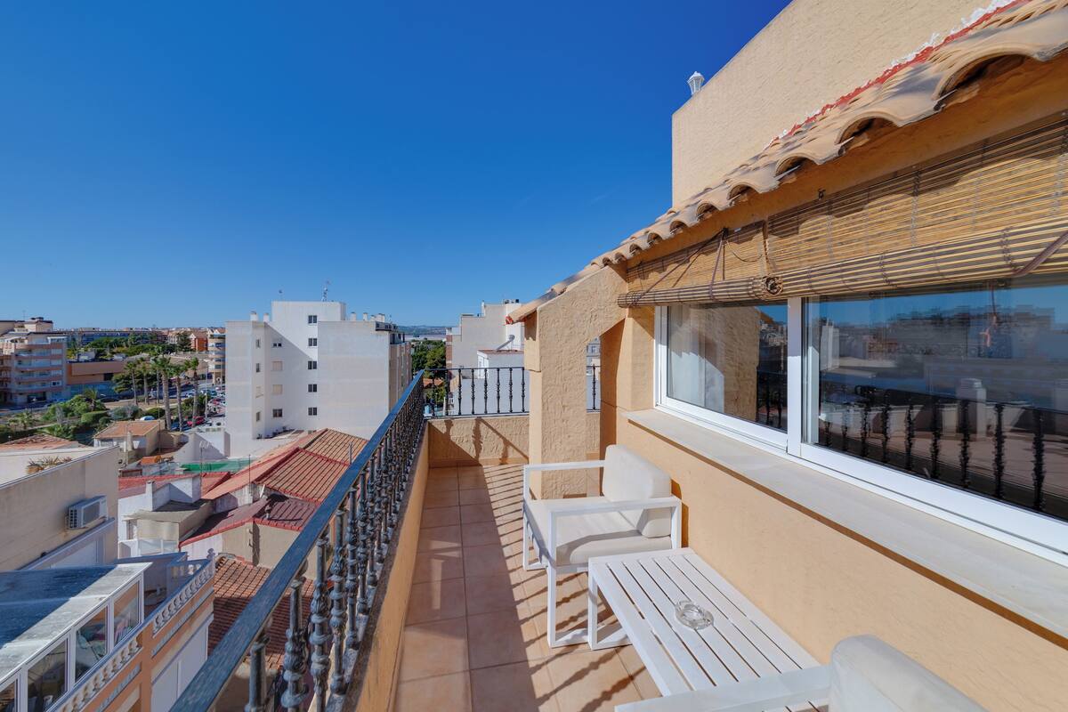 A balcony with white furniture, a view of the city, and a clear blue sky.