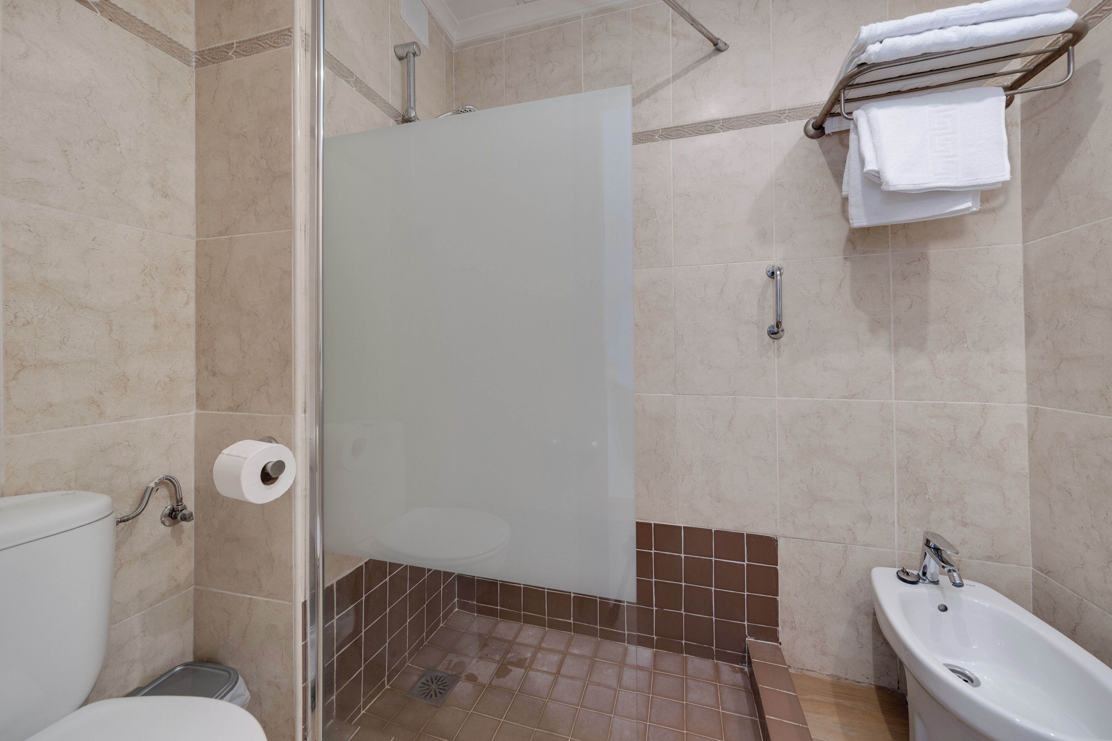 Ein Badezimmer mit Toilette, einer Duschkabine mit Glastür, einem Waschbecken und einem Handtuchhalter.