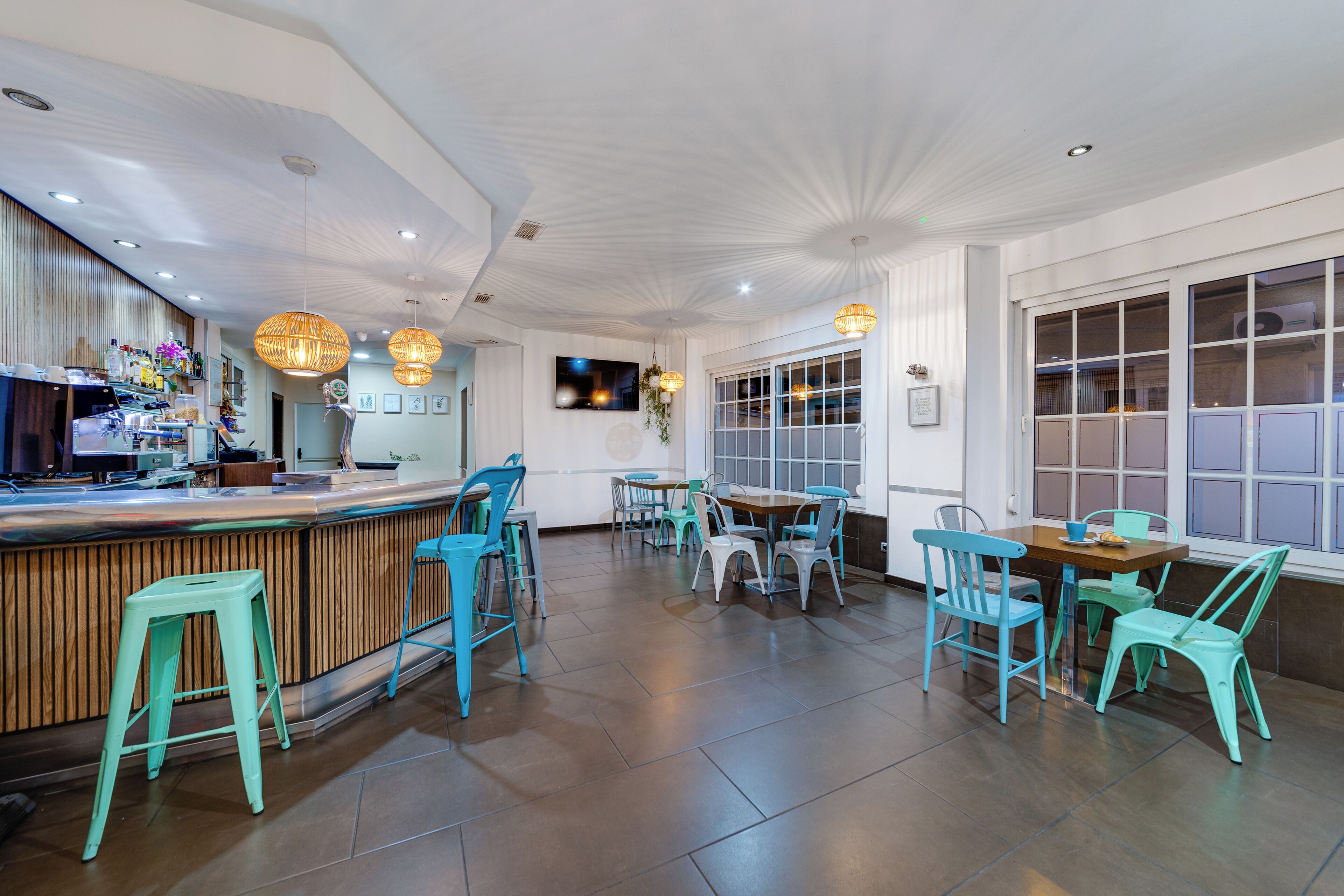 L’intérieur d’un restaurant avec un bar en bois, des chaises de couleur turquoise et une grande fenêtre.
