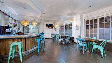 L’intérieur d’un restaurant avec un bar en bois, des chaises de couleur turquoise et une grande fenêtre.