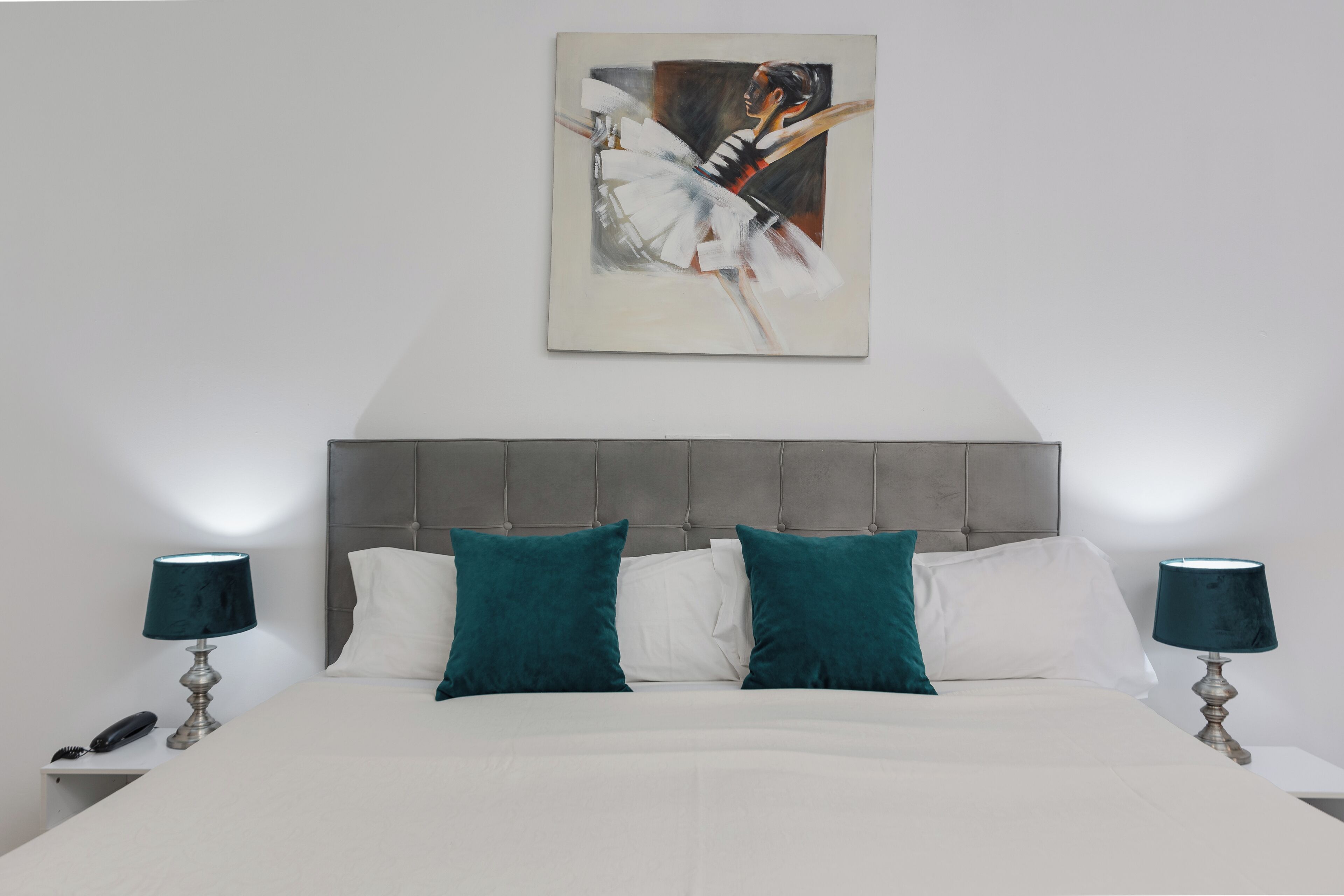 A bedroom with a large bed, two bedside tables with lamps, a headboard, and a painting above the bed.