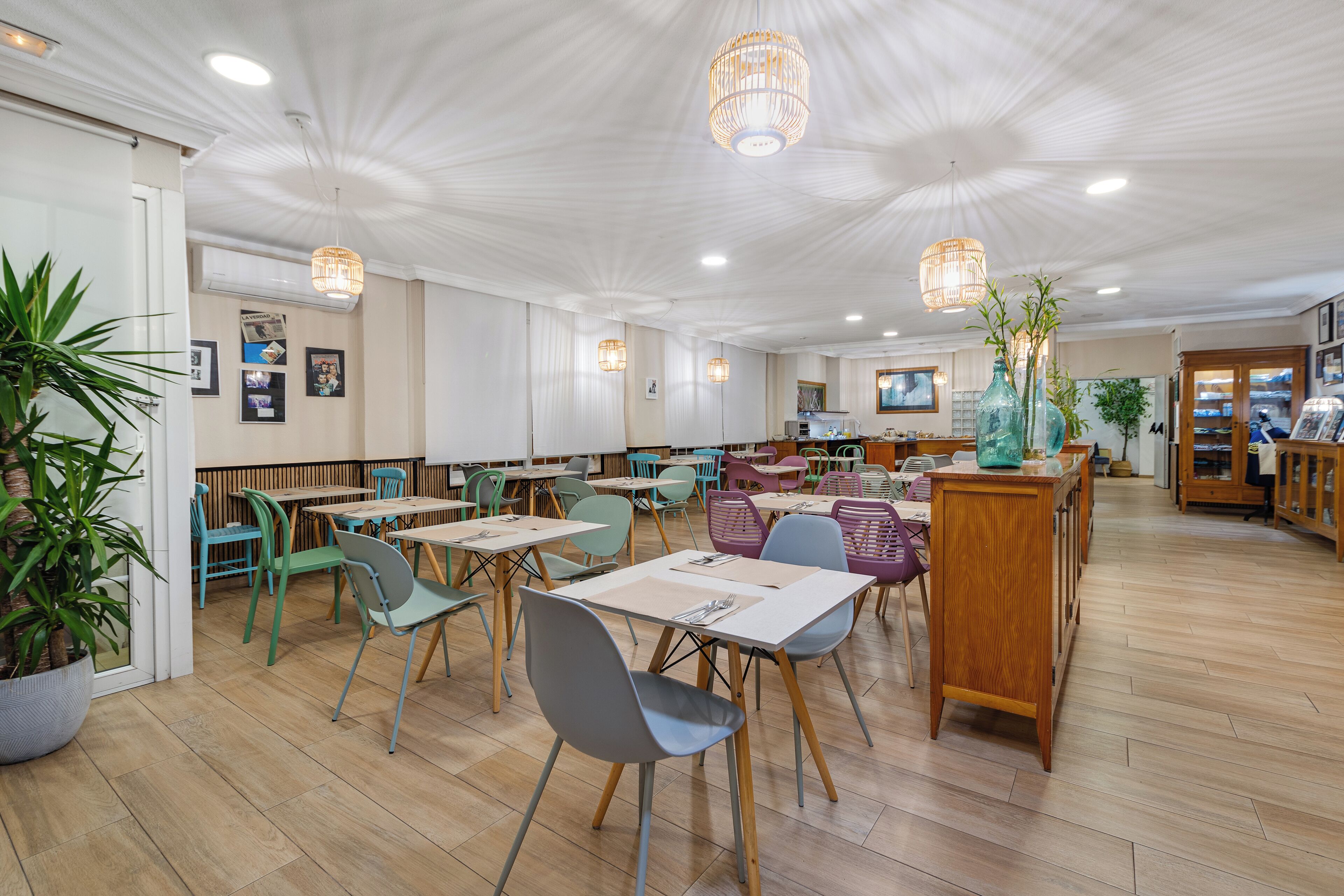 A spacious restaurant with wooden flooring, multiple tables and chairs, and hanging pendant lights.