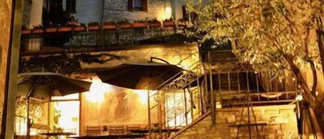 An outdoor seating area with tables and umbrellas, stone walls, and a staircase leading to an upper level.