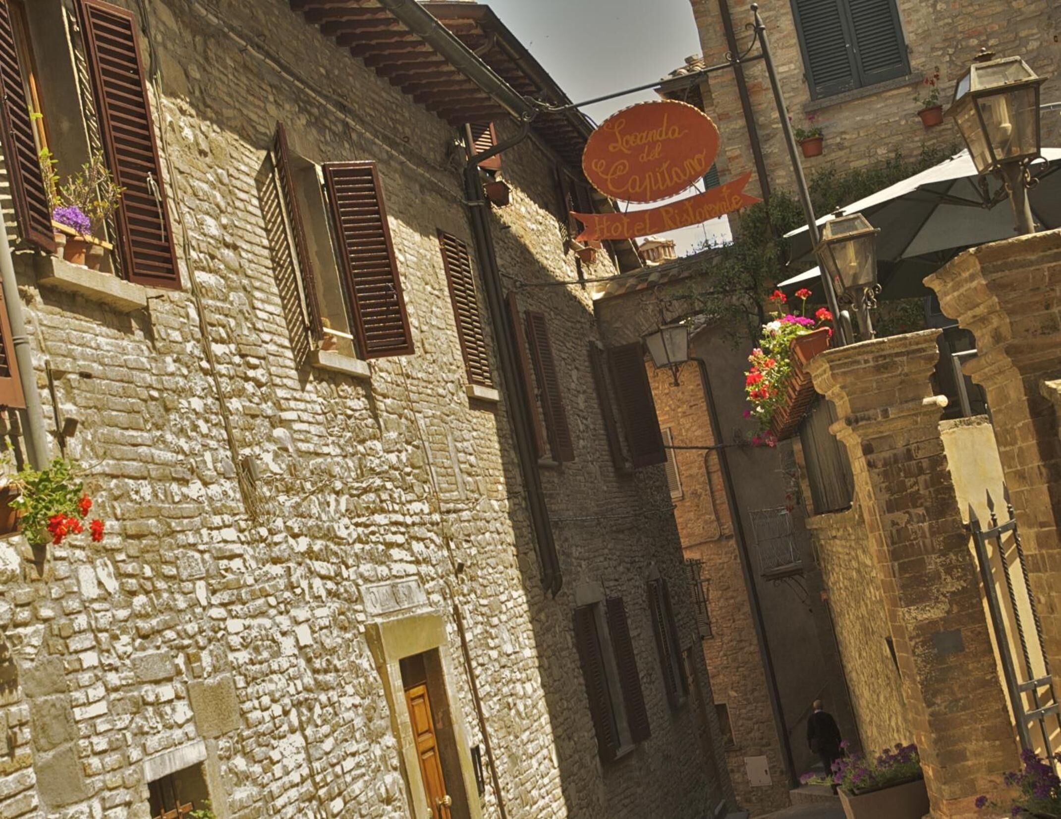 A narrow street with stone buildings, wooden shutters, and hanging flower baskets.
