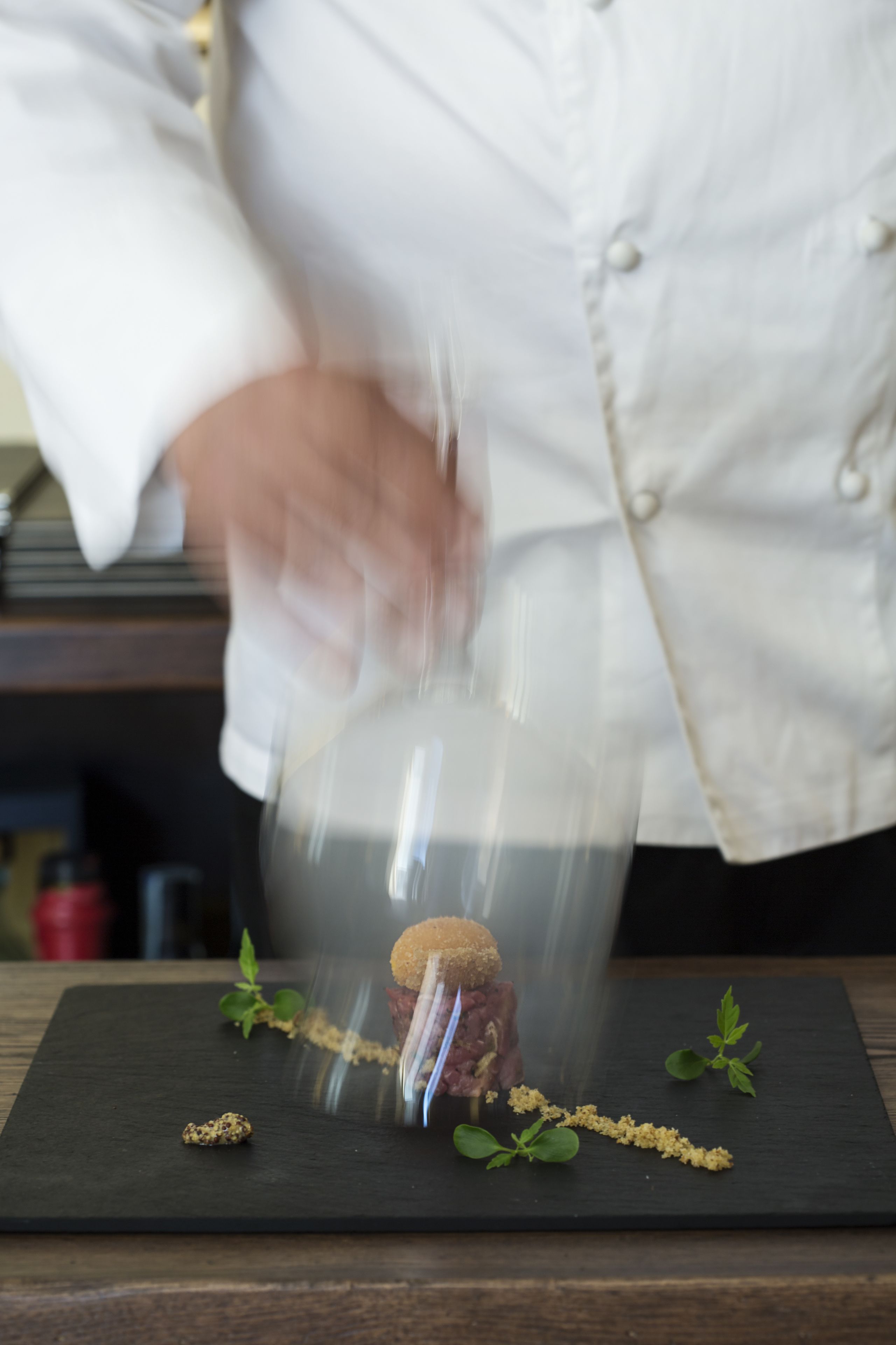 Un chef preparando un plato sobre una tabla de pizarra negra, con énfasis en la comida.