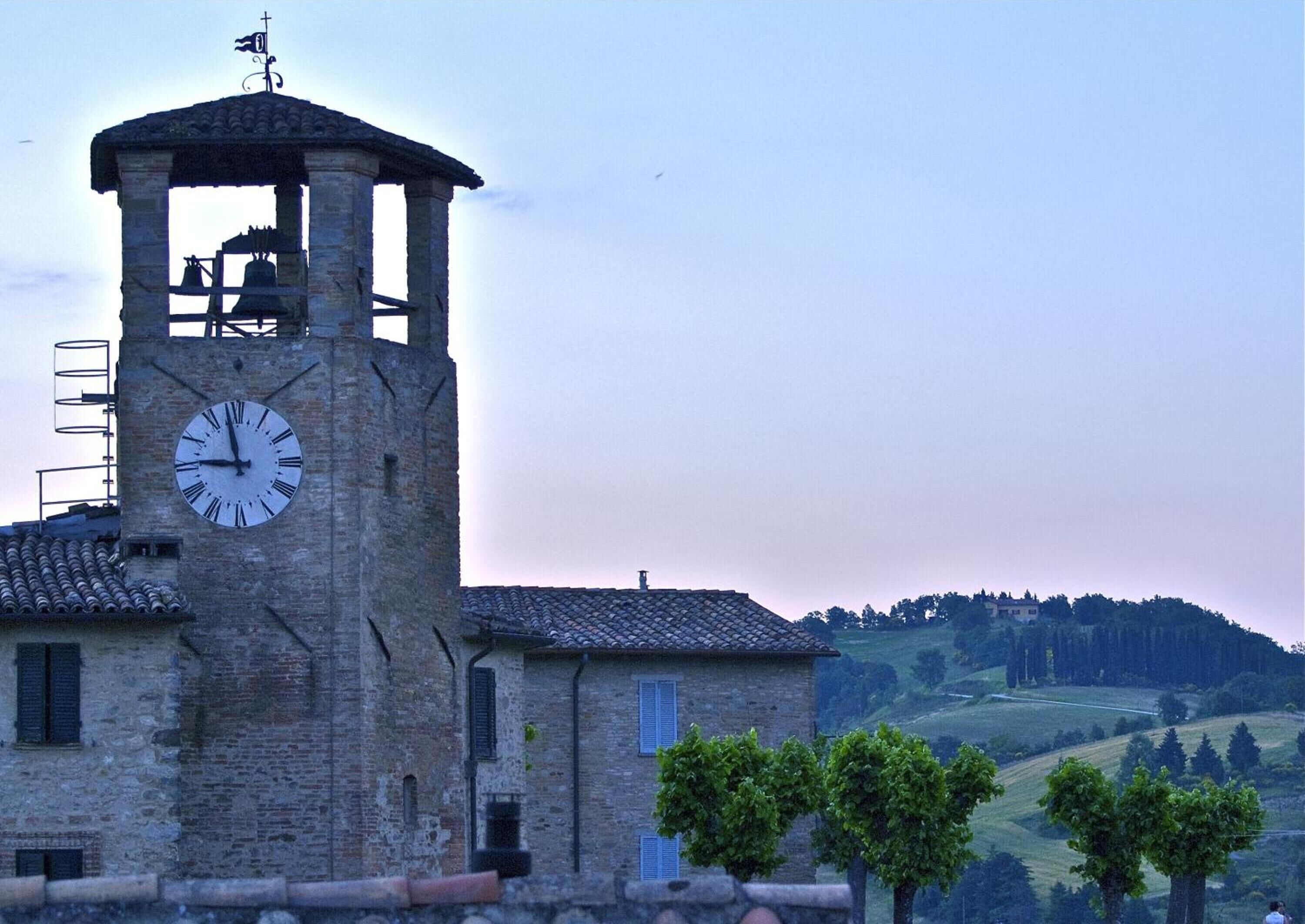 Una torre de piedra histórica con un reloj, una campana y un veleta.