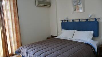 A bedroom with a bed, a headboard, a nightstand, a wall-mounted air conditioner, and a window with curtains.