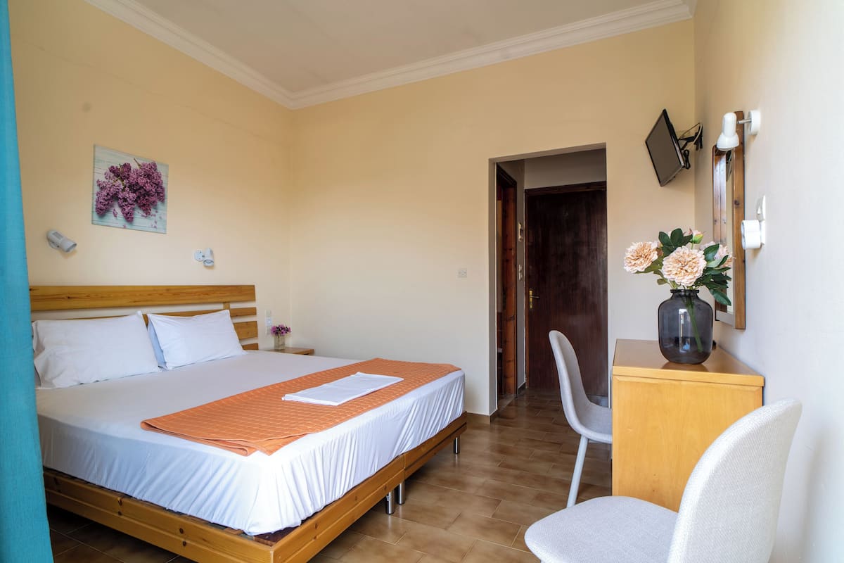 Un dormitorio con cama, una silla, un escritorio y un jarrón con flores.