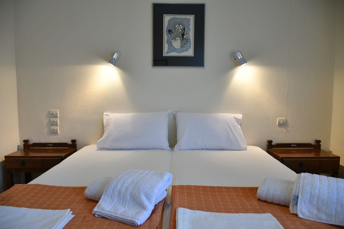Habitación de hotel con dos camas, ropa de cama blanca, un cuadro enmarcado sobre las camas y dos lámparas de noche.