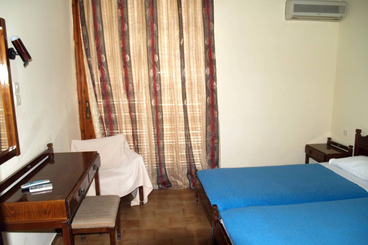Una habitación de hotel con cama, escritorio, silla, espejo y ventana con cortinas.