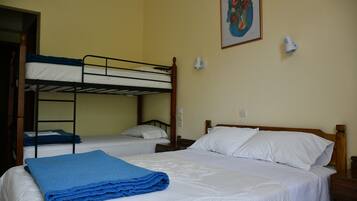 A room with two beds, one with a blue blanket and the other with white bedding. There is a painting on the wall and a small white device on the wall.