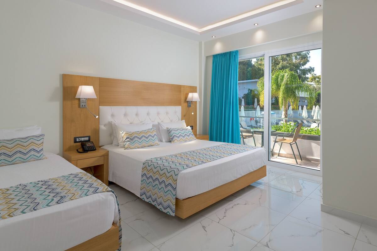 A hotel room with two beds, a wooden headboard, a large window with a view of the outdoors, and a balcony with chairs and umbrellas.