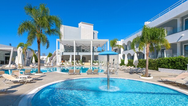 A swimming pool with lounge chairs and umbrellas, surrounded by palm trees and modern buildings. - Oceanis Park Hotel (Rhodes)