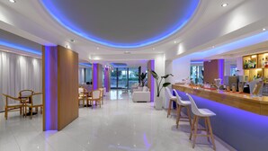 A modern hotel lobby with a bar area, seating, and a view of the outdoors. - Oceanis Park Hotel (Rhodes)