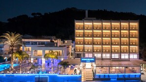 A hotel with multiple floors, a swimming pool, and a well-lit facade. - Oceanis Park Hotel (Rhodes)