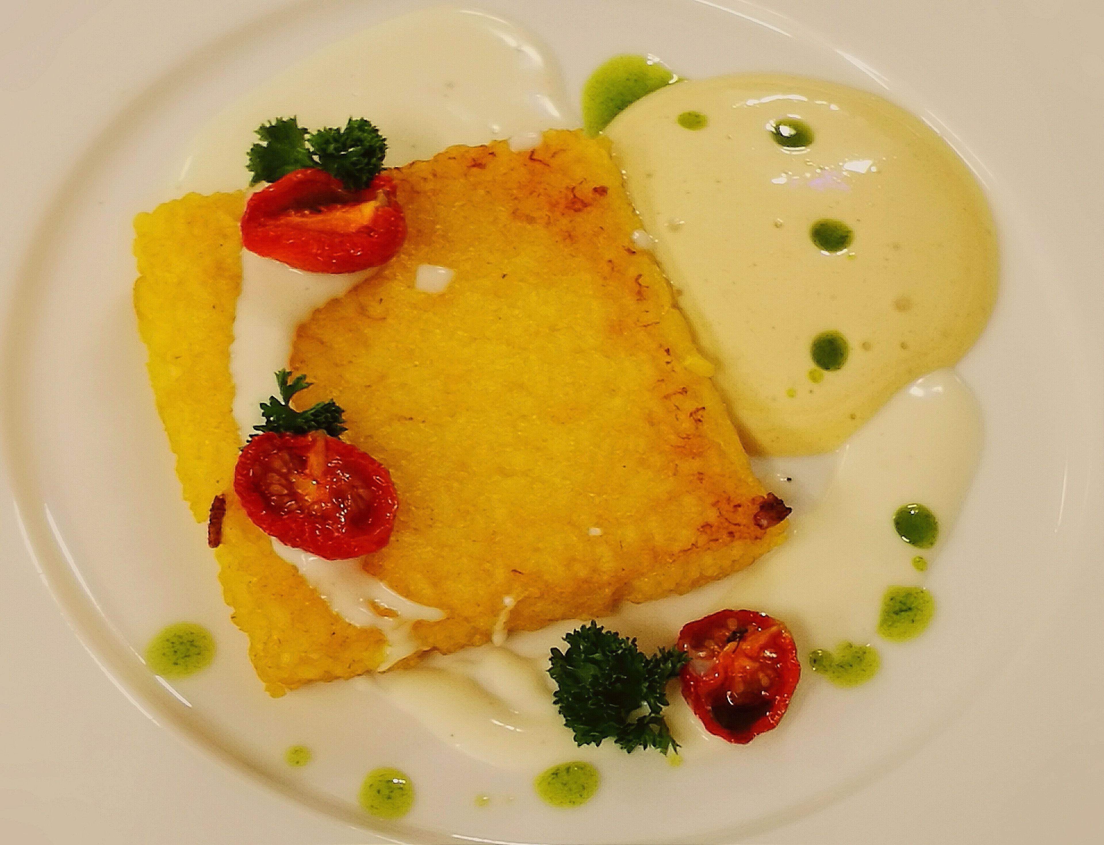 Ein Teller mit paniertem Gericht, vermutlich Hähnchen, garniert mit Petersilie und Cocktailtomaten, begleitet von einer cremigen Soße.