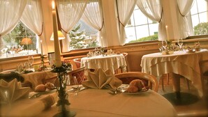 A dining area with tables set for a meal, featuring candlelight and a view of the outdoors. - Piccolo Hotel Andalo Suite Resort (Andalo)
