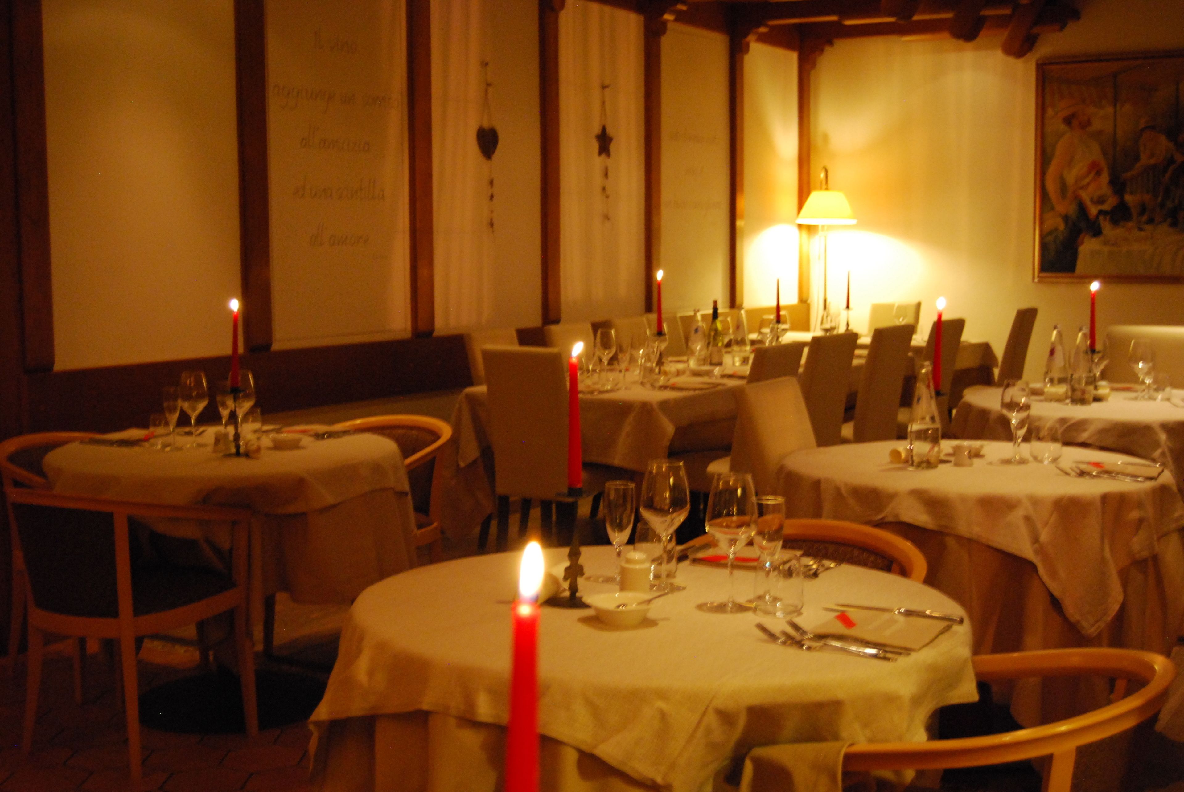 Un restaurant à la lumière tamisée, avec des tables rondes dressées pour le dîner, des bougies et une atmosphère chaleureuse.