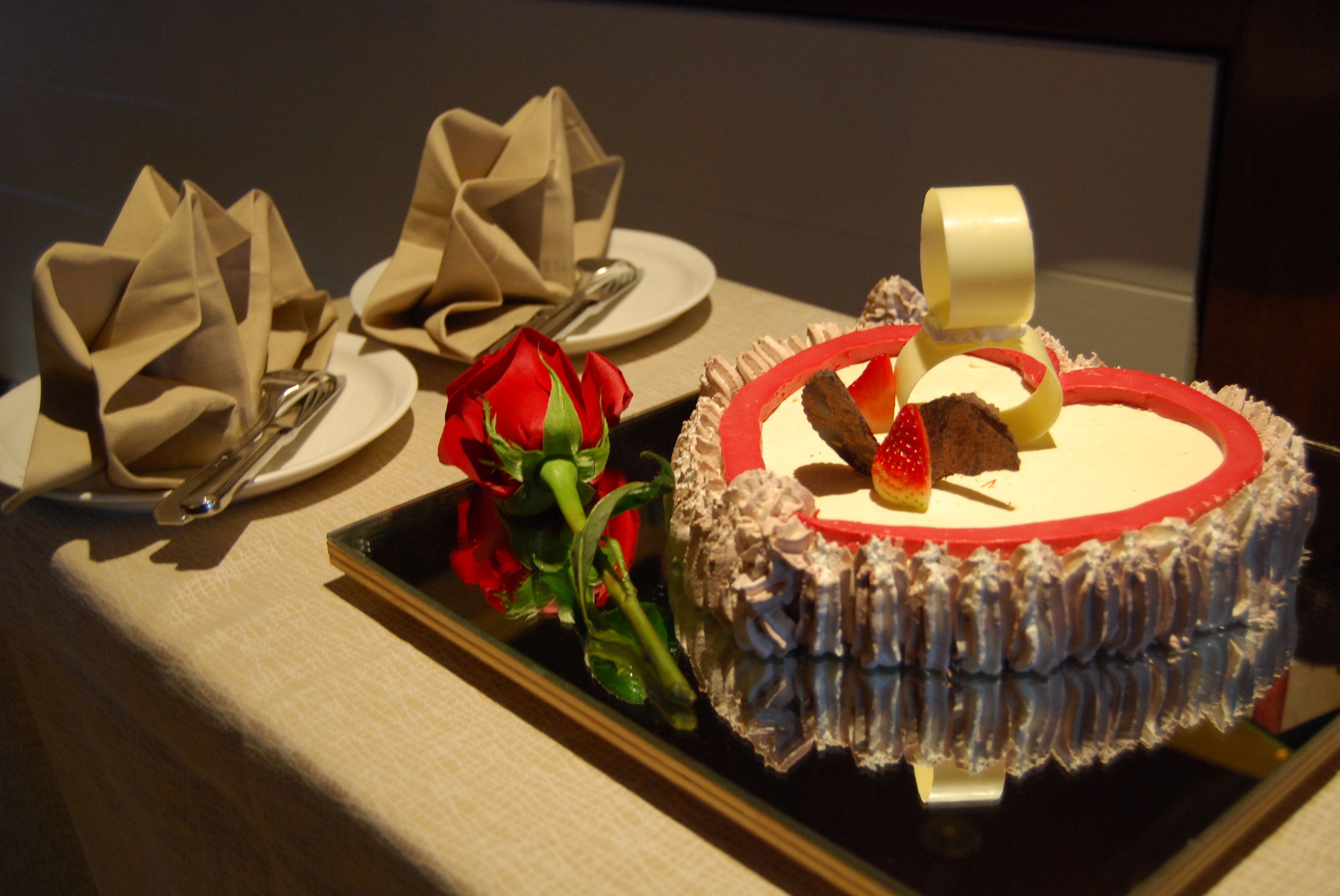 Ein Dessert mit roter Kante und Schokoladenstückchen, begleitet von einer roten Rose und gefalteten Servietten auf einem Tisch.