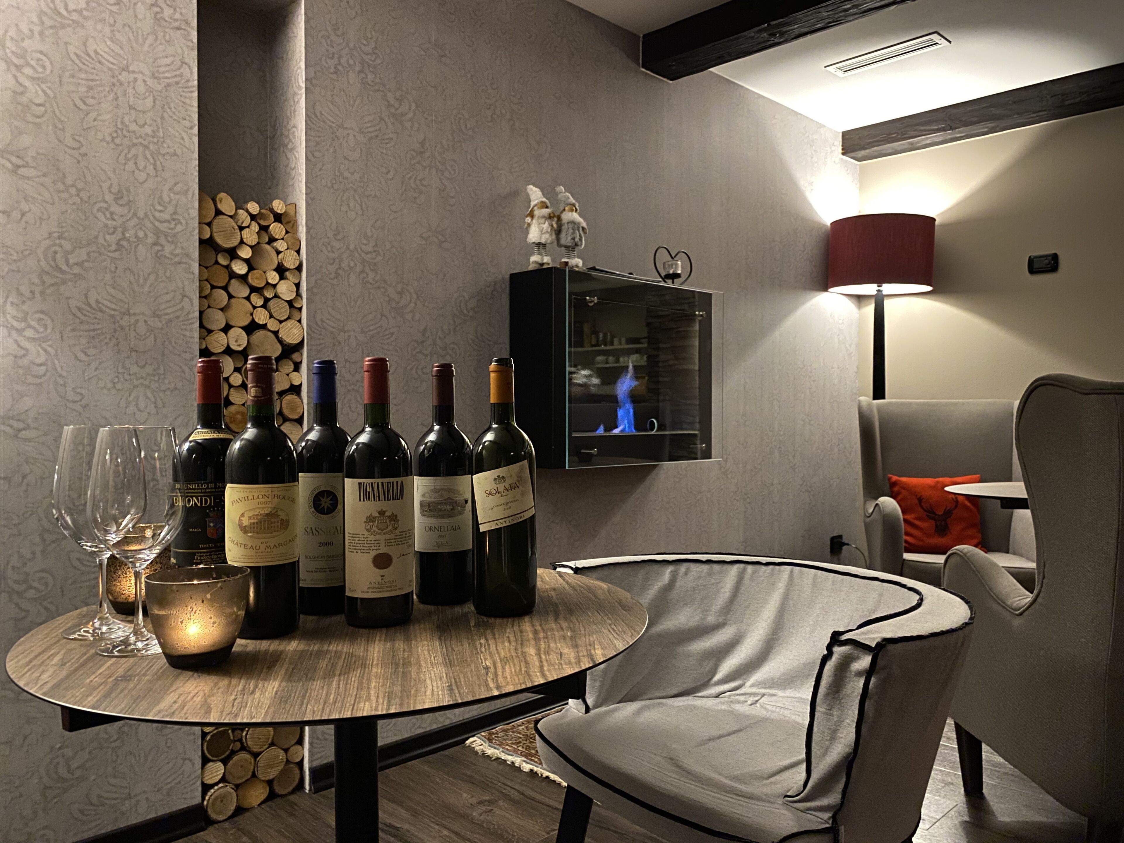 A modern living room with a round wooden table set for a wine tasting, featuring several wine bottles and glasses.