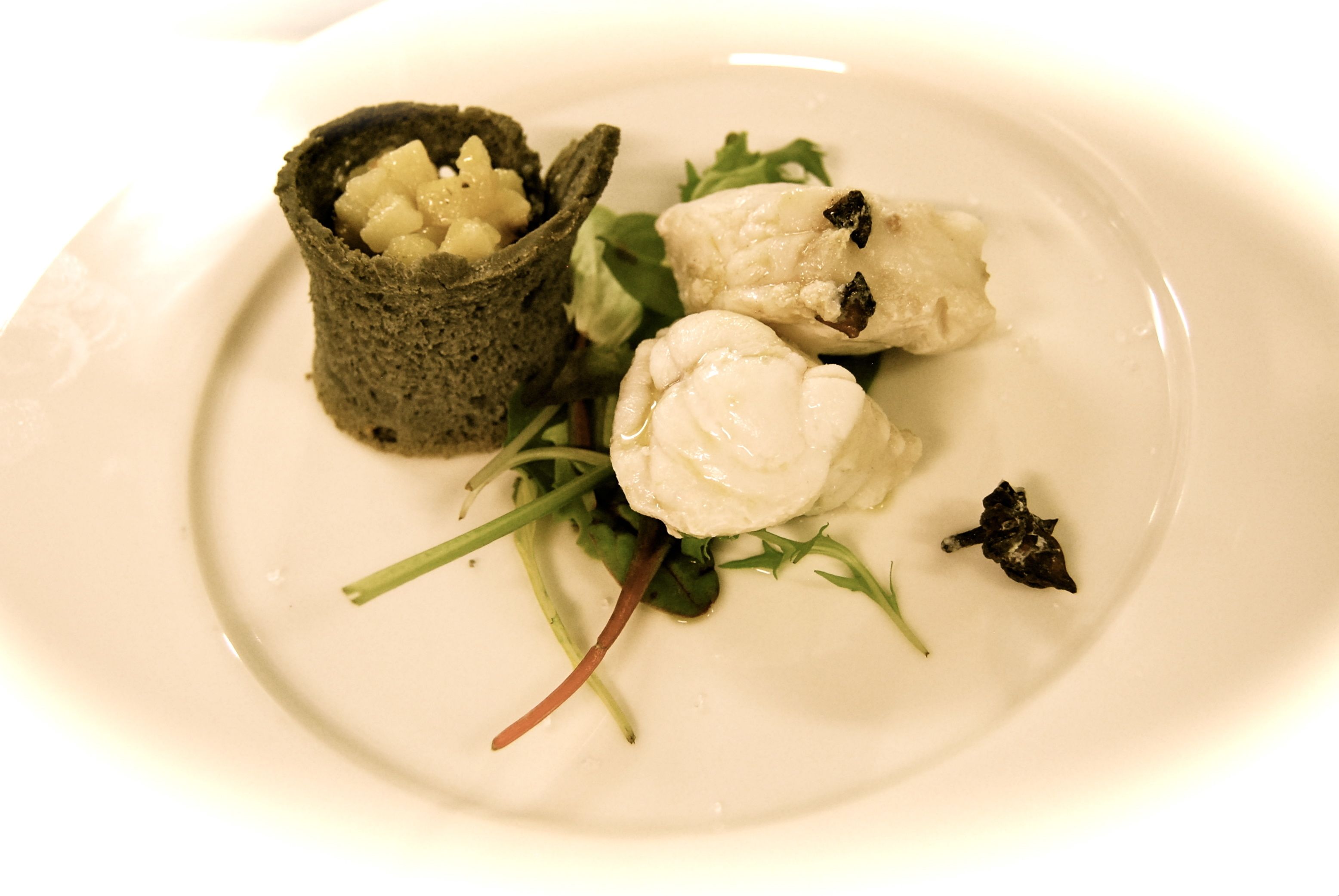 A plate with a food item, possibly a dessert or appetizer, accompanied by greens and a small piece of what appears to be a berry or fruit.