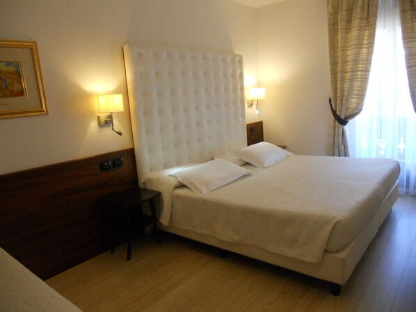 A hotel room with a large bed, two bedside lamps, a wooden headboard, and a framed picture on the wall.