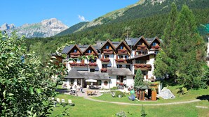 A multi-story hotel with balconies, a garden area, and a mountain backdrop. - Piccolo Hotel Andalo Suite Resort (Andalo)