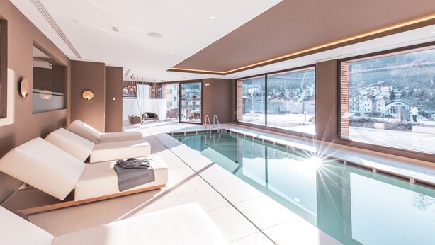 A modern indoor pool area with lounge chairs and a view of a snowy landscape. - Piccolo Hotel Andalo Suite Resort (Andalo)