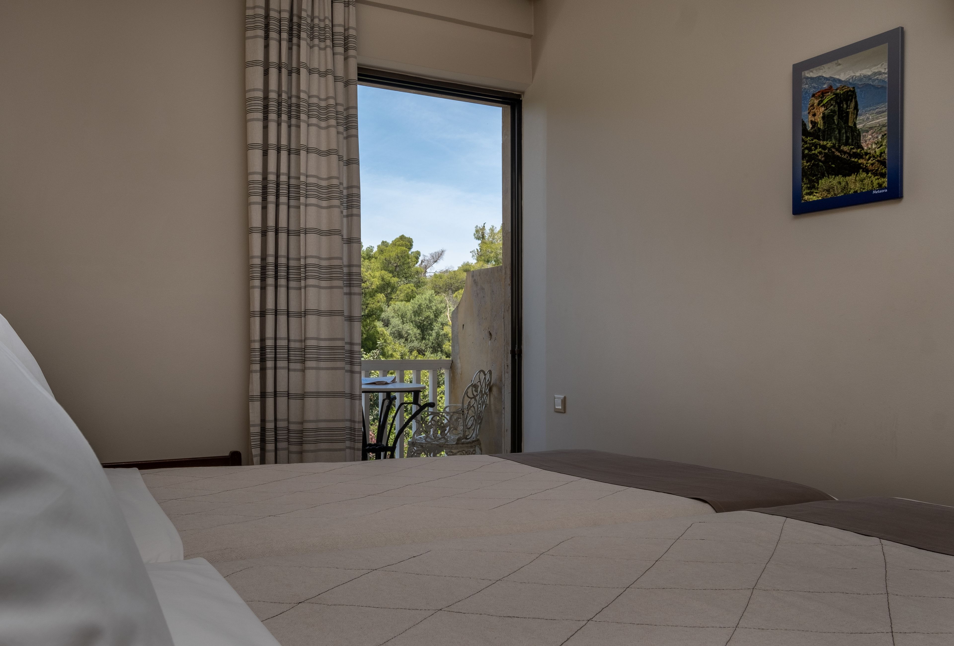 A bedroom with a large bed, a view of a balcony, and a painting on the wall.