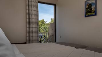 A bedroom with a large bed, a view of a balcony, and a painting on the wall.