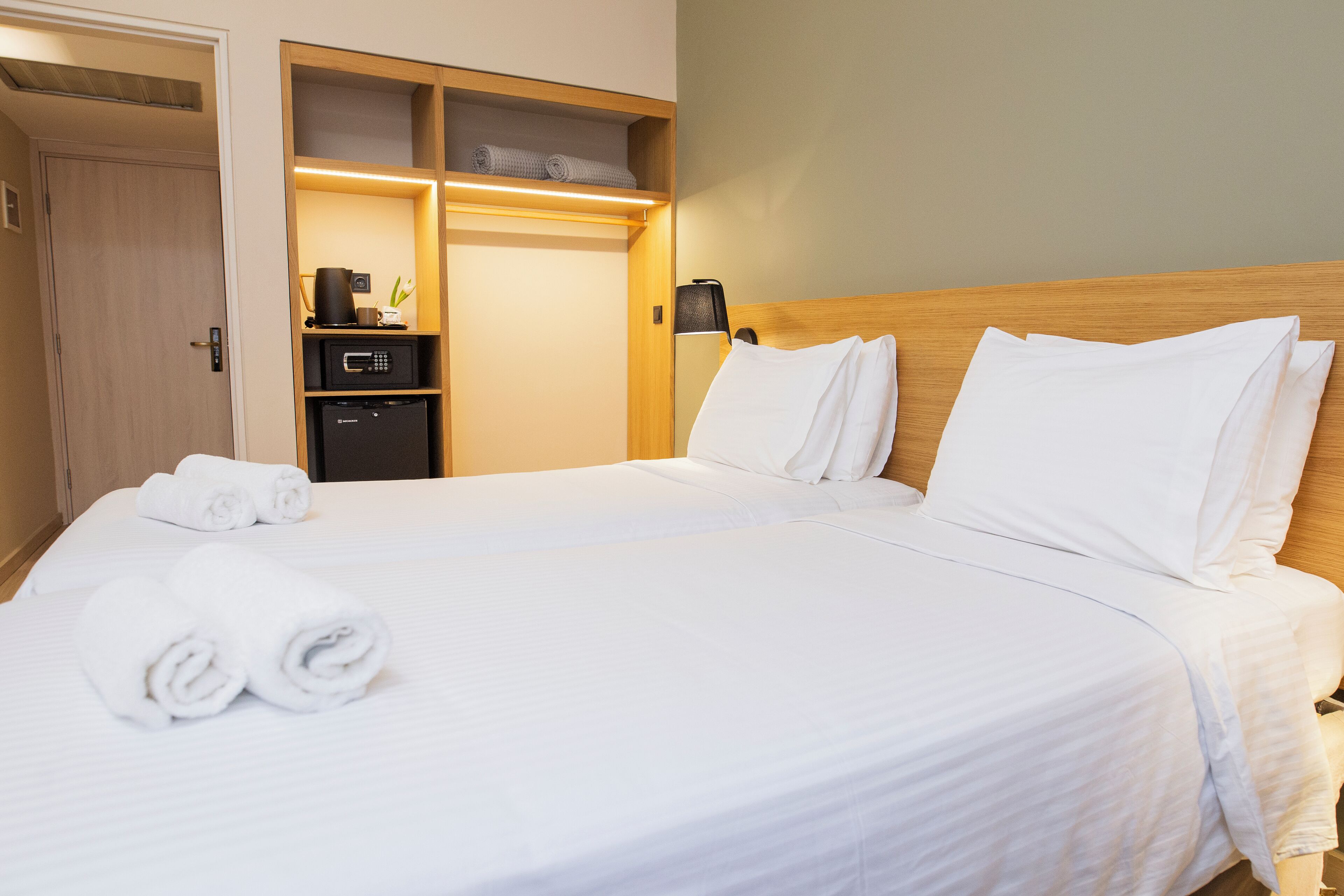 A hotel room with a neatly made bed, a minibar, and a wooden headboard.
