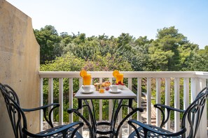 A balcony with a table set for breakfast, surrounded by chairs, overlooking a forested area.