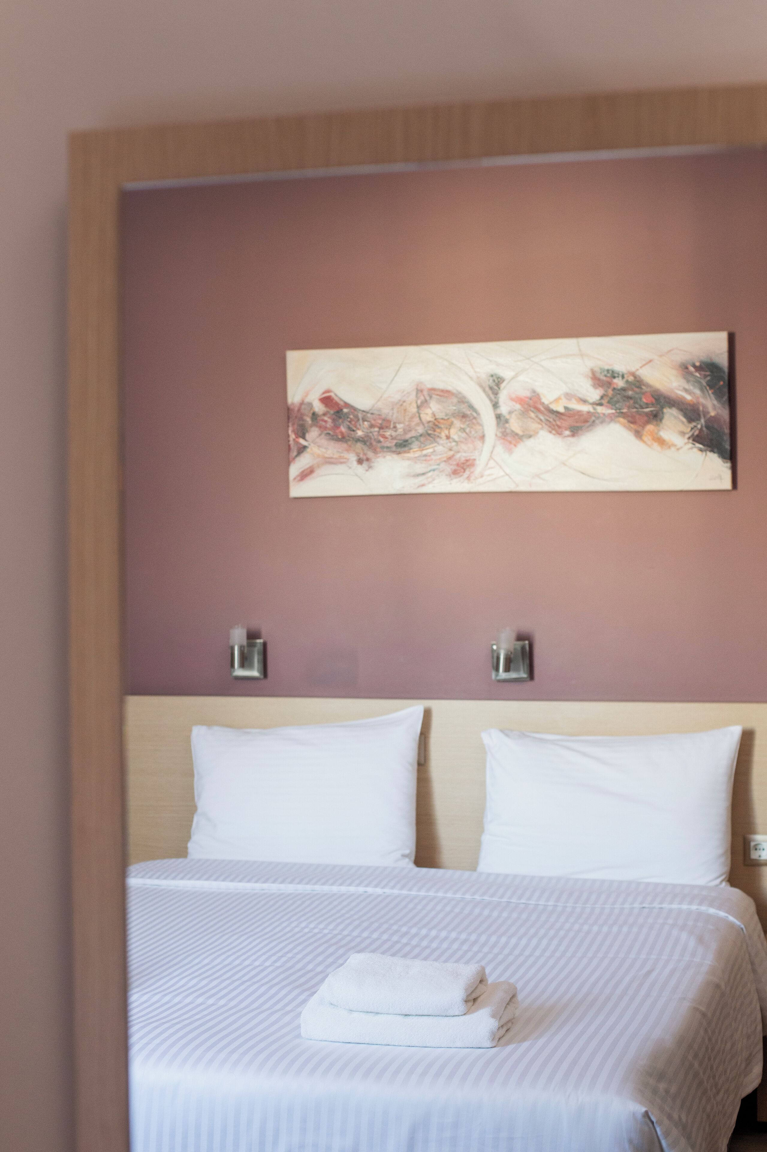 Une chambre d’hôtel avec un lit, deux oreillers, une serviette pliée et un tableau abstrait accroché au mur.
