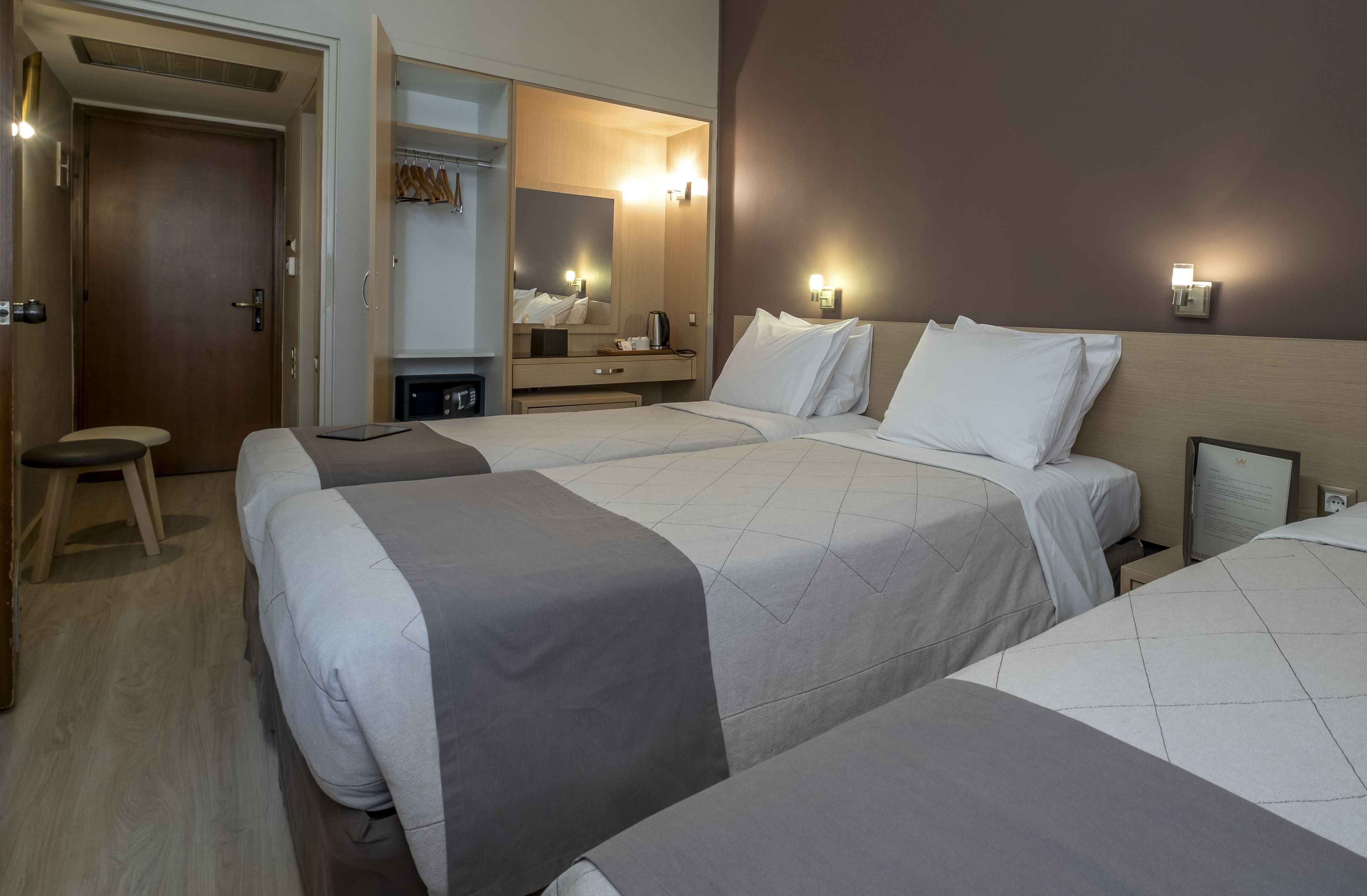 Habitación de hotel con dos camas, una mesita de noche, una silla, un armario y un espejo.