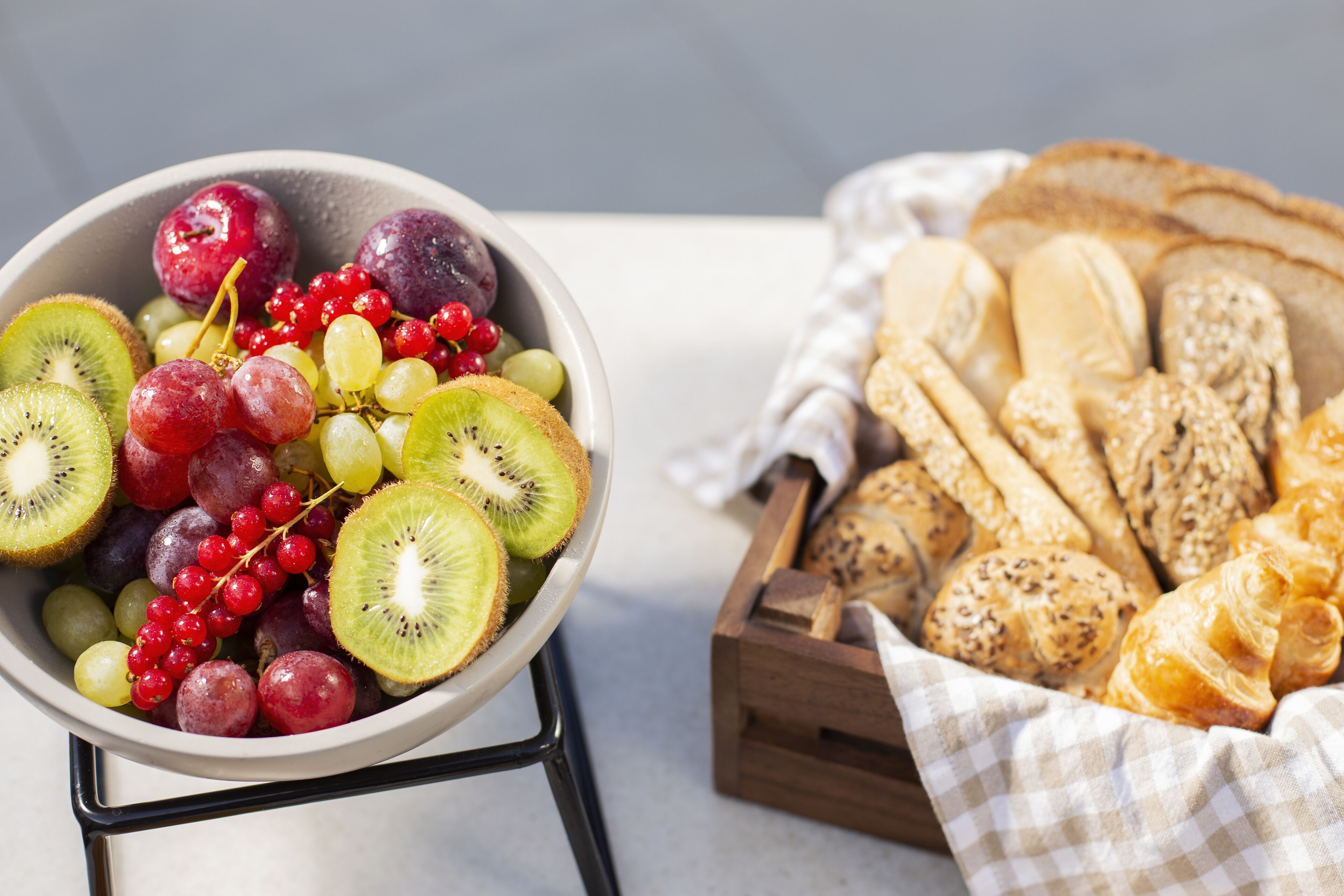 A bowl of assorted fruits and a wooden basket of bread.