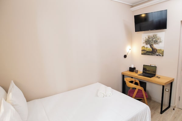 A hotel room with a bed, a desk with a laptop, a chair, a TV mounted on the wall, and a framed picture of a tree. - Acropolis View Hotel (Athens)