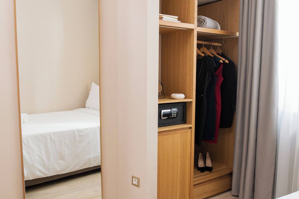 Un dormitorio con cama, armario, espejo y escritorio con lámpara.