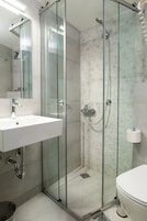 Uma casa de banho moderna com chuveiro em cabine de vidro, lavatório branco e sanita.