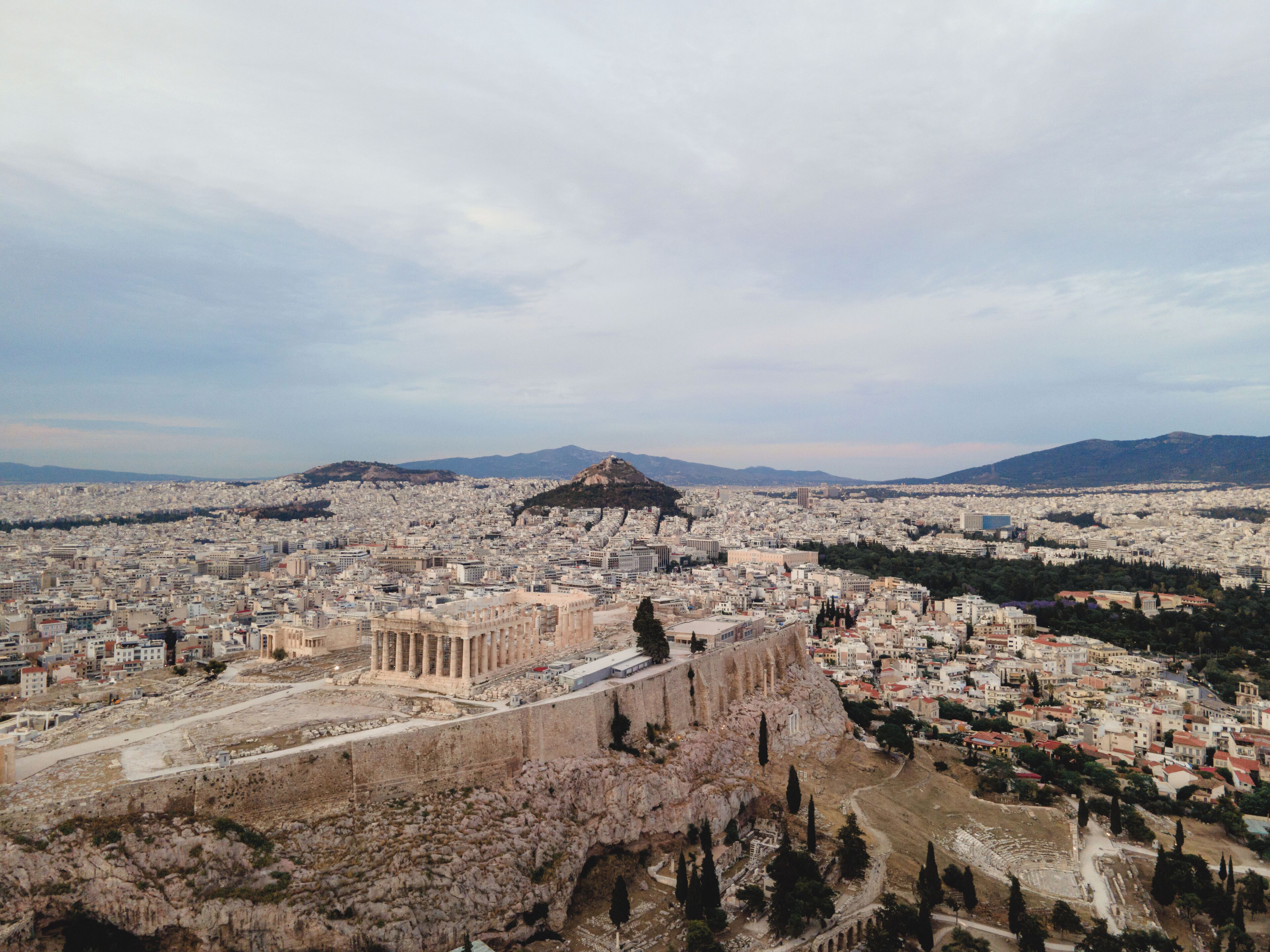 A panoramic view of a city with ancient ruins in the foreground and a mountain in the background.