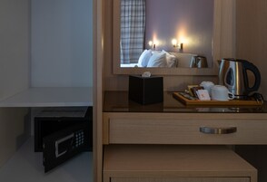 A hotel room with a wooden cabinet, a microwave, a tray with a kettle, cups, and a small box.