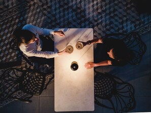 A top-down view of a dining table with two chairs, a person holding a cup, and another person with a cup on the table.