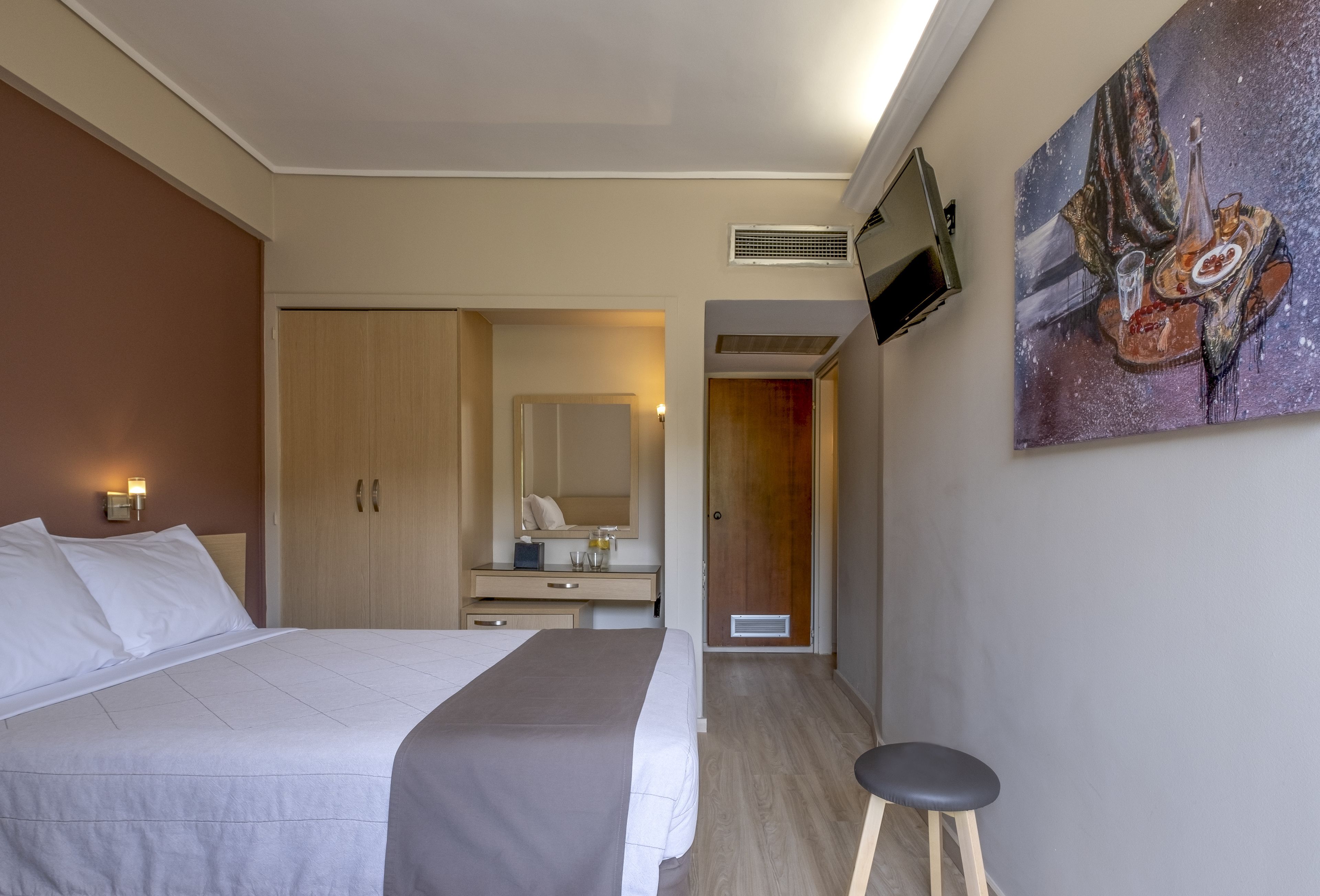 Habitación de hotel con cama, escritorio con espejo, televisor montado en la pared y un cuadro.
