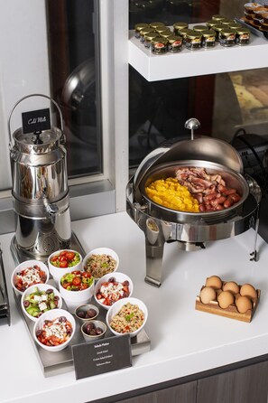 A buffet setup with various food items, including a coffee pot, a hot dish with meats and vegetables, and several bowls of salads and other dishes.