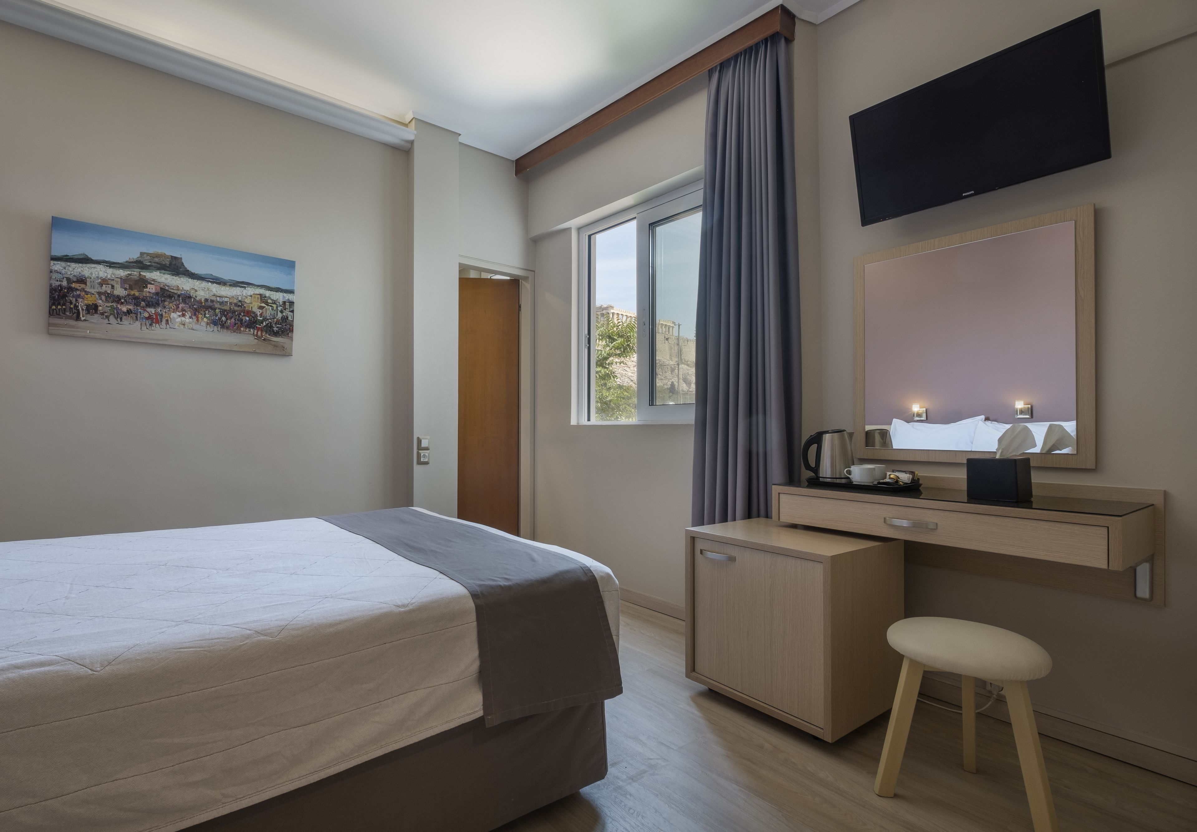 Ein Hotelzimmer mit Bett, Schreibtisch mit Spiegel, Fernseher über dem Schreibtisch und Fenster mit Vorhängen.