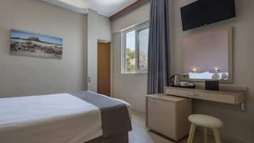 Ein Hotelzimmer mit Bett, Schreibtisch mit Spiegel, Fernseher über dem Schreibtisch und Fenster mit Vorhängen.