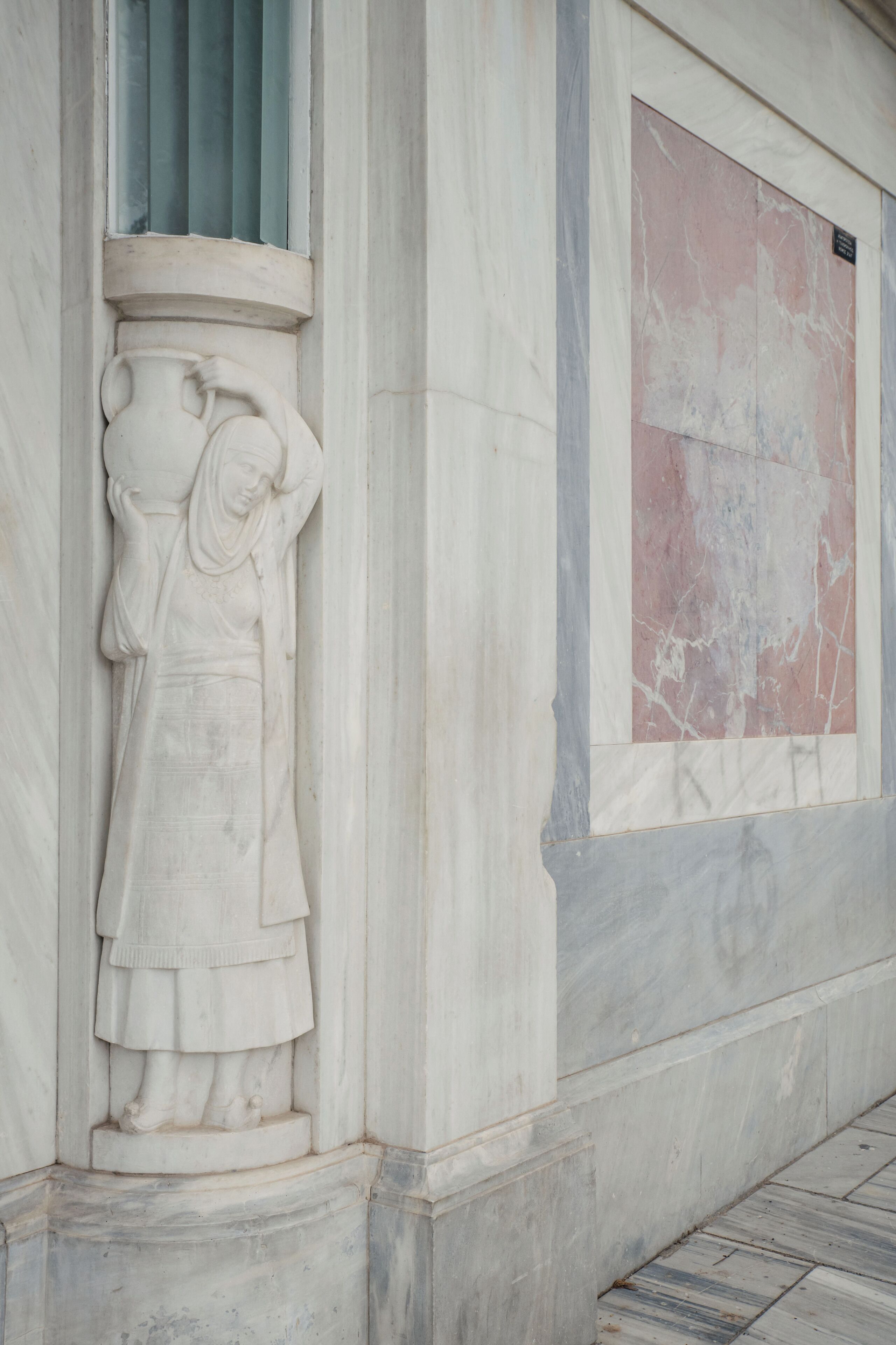 A marble statue of a woman with a draped garment, set in a column base, against a wall with a marble panel.