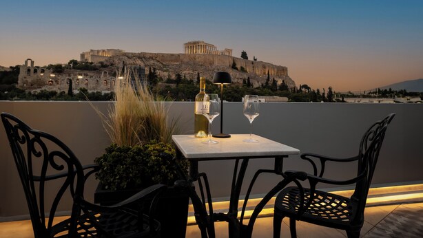 A table with two wine glasses and a bottle, overlooking ancient ruins. - Acropolis View Hotel (Athens)